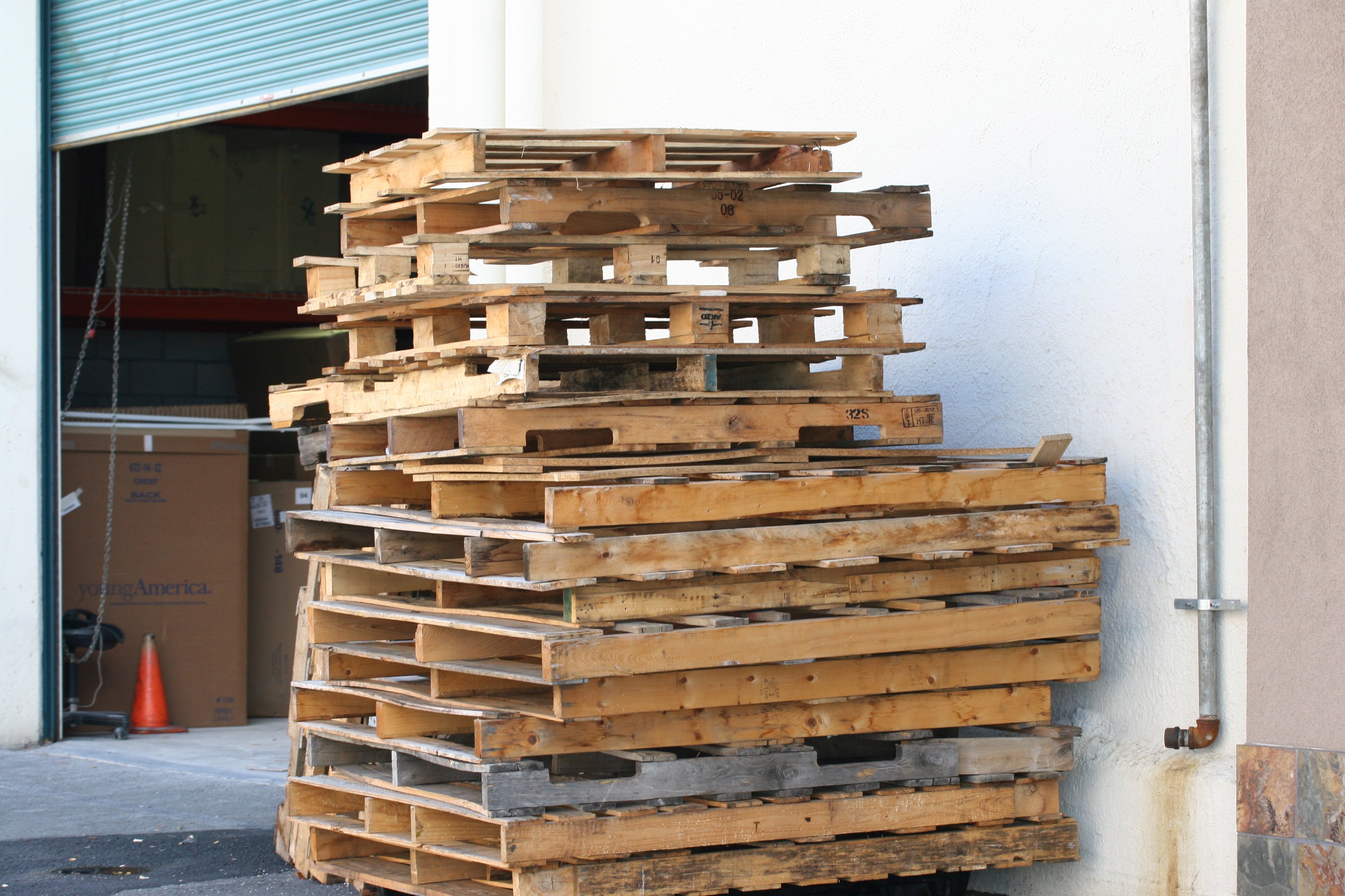 Tall stack of mixed used wooden pallets ready for pickup at a loading dock